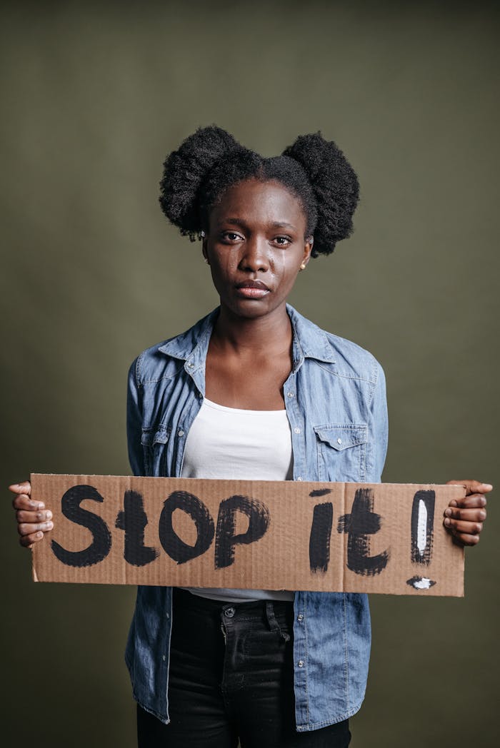 Black woman in a studio holding a protest sign with 'Stop it!' message.